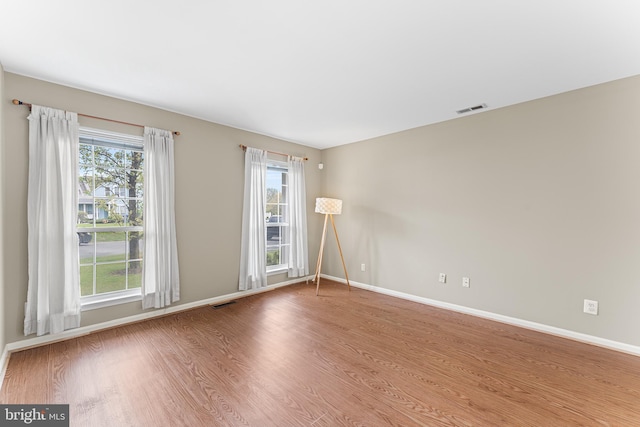 empty room featuring wood finished floors, visible vents, and baseboards