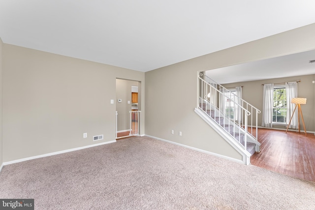 carpeted empty room featuring baseboards, stairs, and visible vents