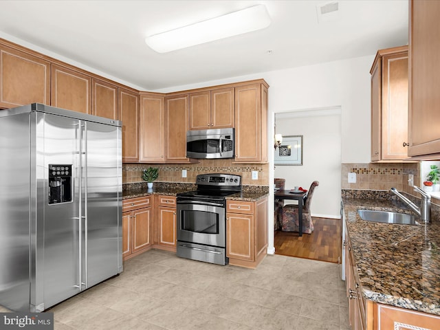kitchen with a sink, dark stone counters, stainless steel appliances, light tile patterned floors, and tasteful backsplash