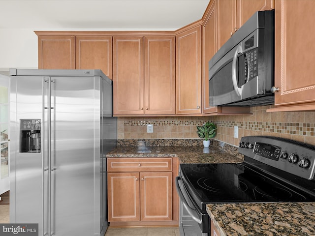 kitchen featuring brown cabinetry, tasteful backsplash, dark stone counters, stainless steel appliances, and light tile patterned flooring