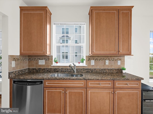 kitchen featuring stainless steel dishwasher, backsplash, a sink, and dark stone countertops