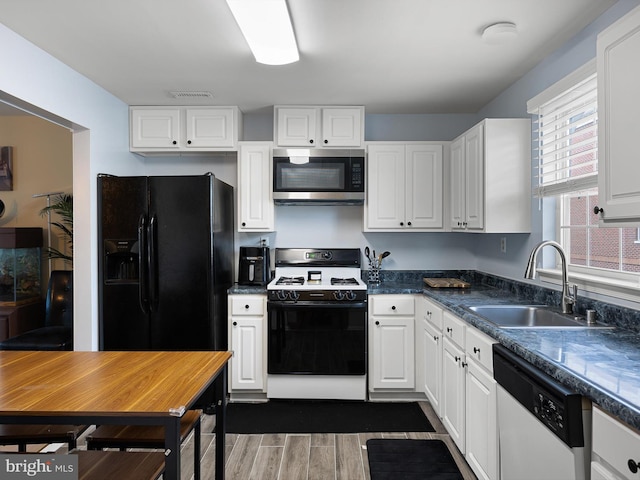 kitchen featuring dishwasher, a sink, stainless steel microwave, gas range, and black fridge