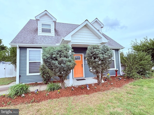 cape cod house featuring a front yard, roof with shingles, and fence