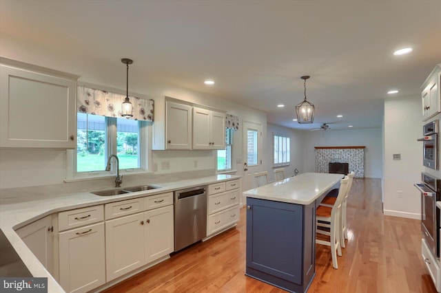 kitchen featuring a ceiling fan, a sink, light wood-style flooring, a fireplace, and appliances with stainless steel finishes