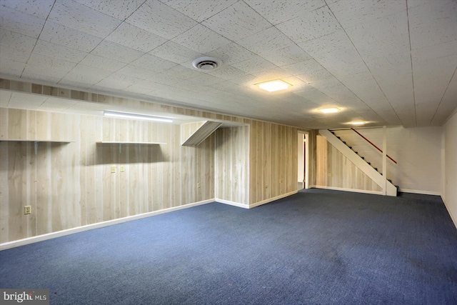 finished below grade area with stairway, visible vents, dark carpet, and wooden walls