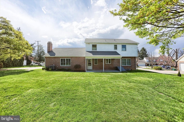 back of property with brick siding, a lawn, central AC, and a chimney