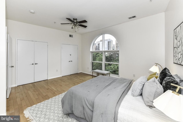 bedroom featuring hardwood / wood-style floors, multiple closets, baseboards, and a ceiling fan