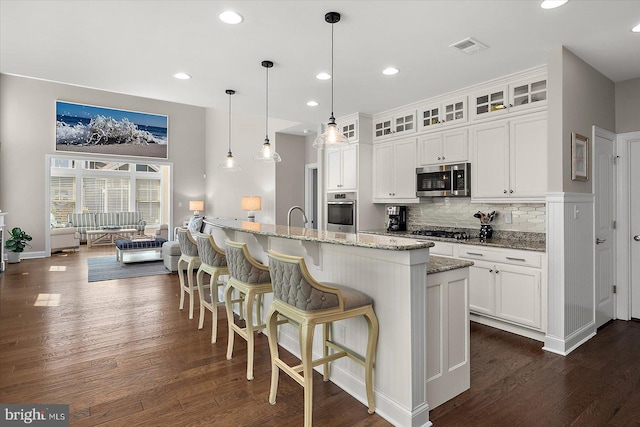 kitchen with light stone counters, backsplash, appliances with stainless steel finishes, and dark wood-type flooring