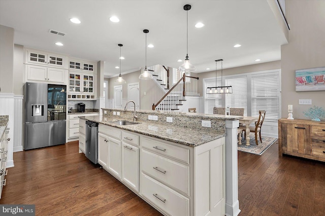kitchen with an island with sink, stainless steel appliances, visible vents, a sink, and glass insert cabinets