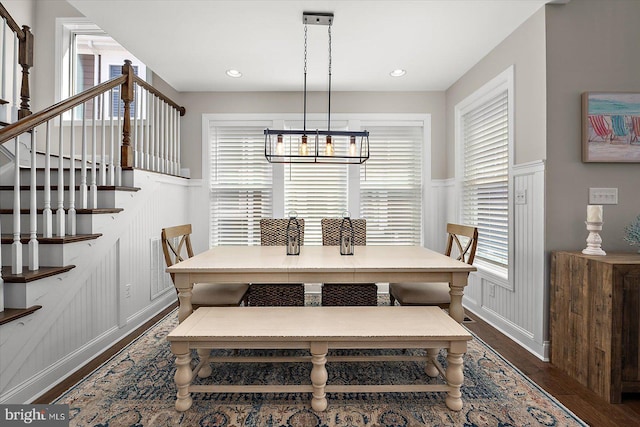 dining space with stairway, a decorative wall, a chandelier, a wainscoted wall, and dark wood finished floors