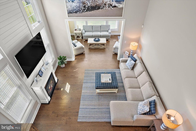 living room featuring a warm lit fireplace, wood finished floors, and baseboards
