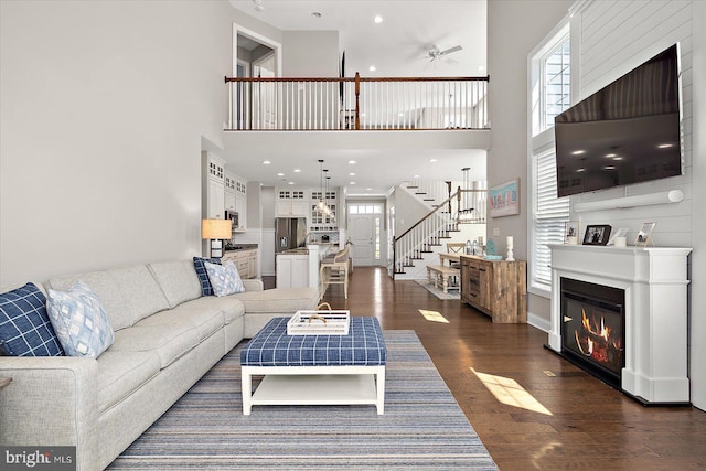 living room with plenty of natural light, stairway, a towering ceiling, and ceiling fan