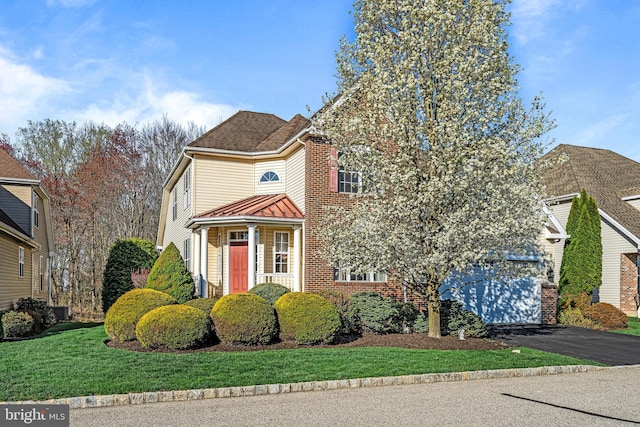 traditional home with driveway, a standing seam roof, metal roof, a front yard, and brick siding