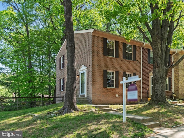 colonial inspired home with entry steps, fence, brick siding, and a front yard