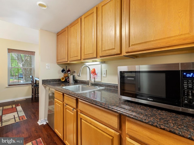 kitchen with a sink, dark stone counters, stainless steel appliances, dark wood-type flooring, and baseboards