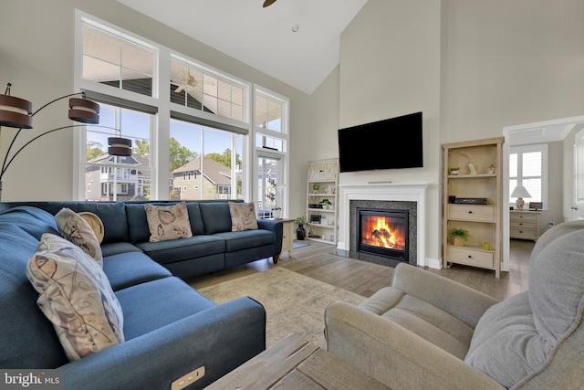 living area featuring ceiling fan, high vaulted ceiling, a fireplace with flush hearth, and wood finished floors