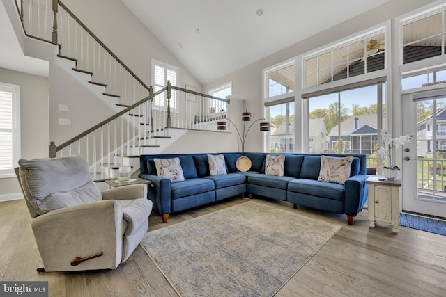 living area featuring high vaulted ceiling, baseboards, stairs, and wood finished floors