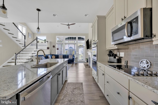 kitchen with decorative backsplash, light wood-style floors, a sink, appliances with stainless steel finishes, and hanging light fixtures