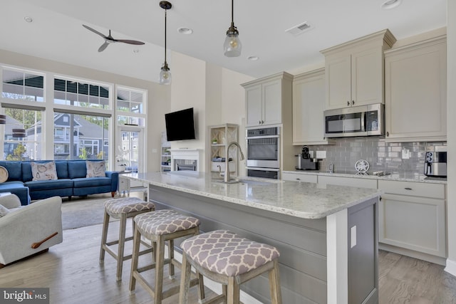 kitchen featuring stainless steel appliances, open floor plan, light stone countertops, and tasteful backsplash