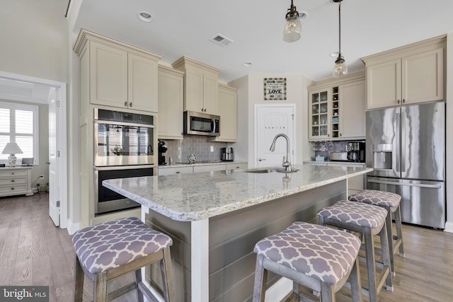 kitchen with cream cabinets, appliances with stainless steel finishes, a sink, and tasteful backsplash