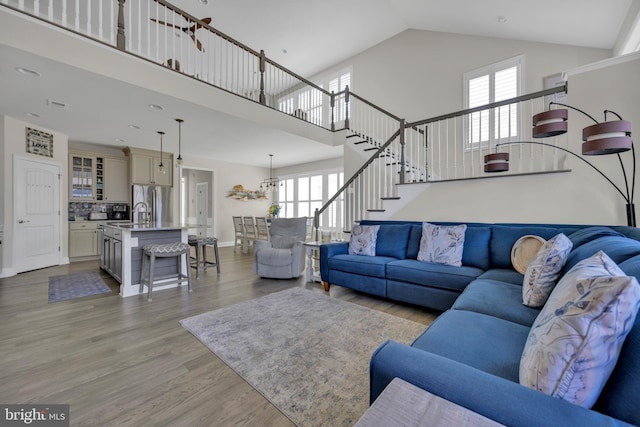 living room with light wood-style floors, a wealth of natural light, high vaulted ceiling, and stairway