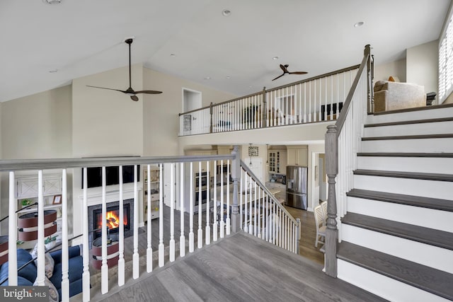 staircase featuring ceiling fan, a warm lit fireplace, and wood finished floors
