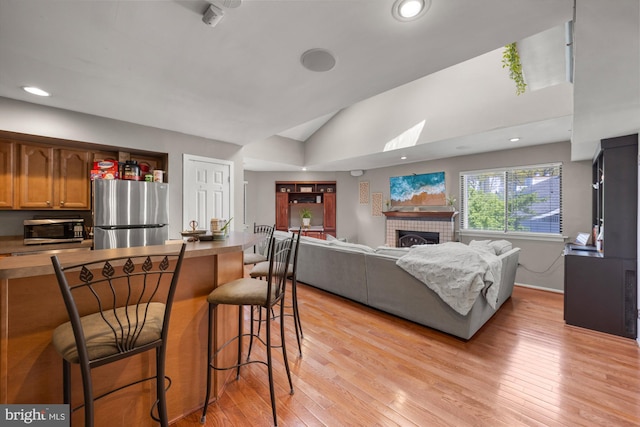living area with lofted ceiling, a brick fireplace, recessed lighting, and light wood-style floors