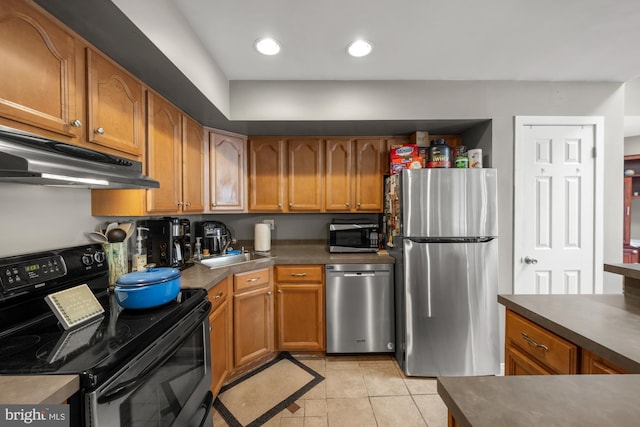 kitchen featuring brown cabinets, under cabinet range hood, dark countertops, light tile patterned floors, and appliances with stainless steel finishes