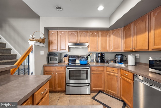 kitchen featuring under cabinet range hood, stainless steel appliances, dark countertops, a sink, and light tile patterned flooring