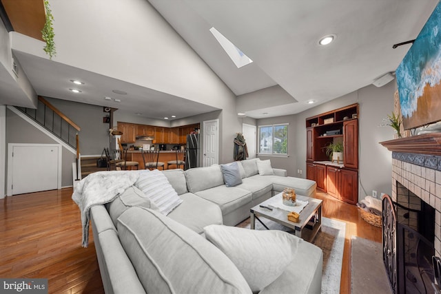 living room with recessed lighting, light wood-style floors, a skylight, a brick fireplace, and stairs