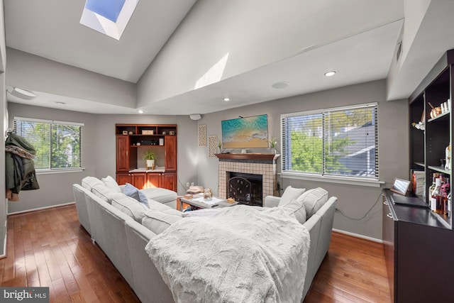 living area with lofted ceiling with skylight, a tiled fireplace, baseboards, and dark wood-style floors