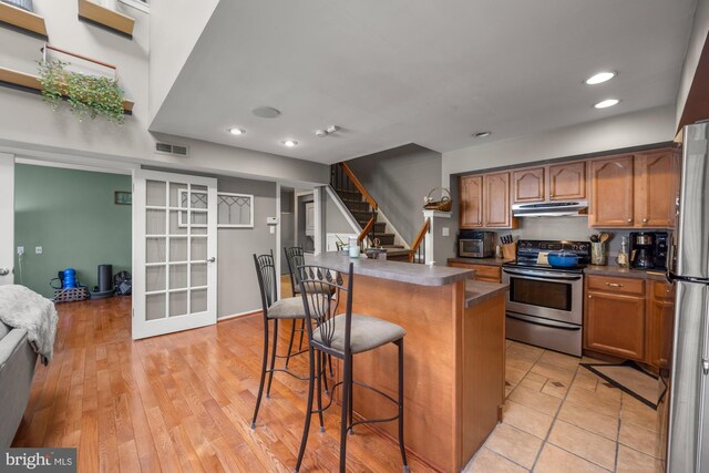 kitchen featuring french doors, stainless steel appliances, a kitchen bar, under cabinet range hood, and visible vents
