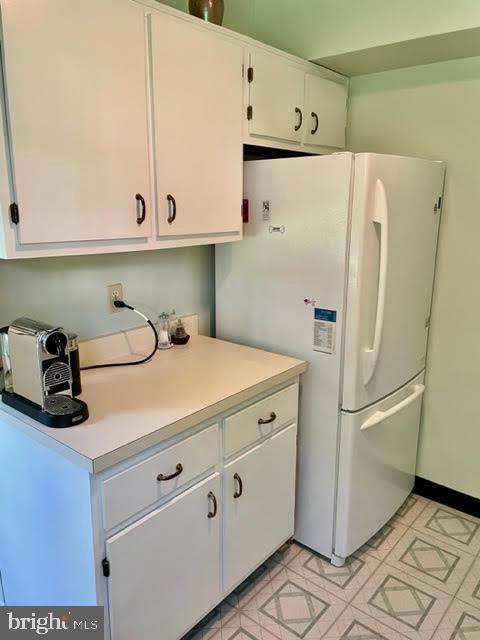kitchen with light floors, freestanding refrigerator, white cabinetry, and light countertops