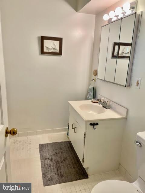 half bath featuring vanity, tile patterned floors, baseboards, and toilet