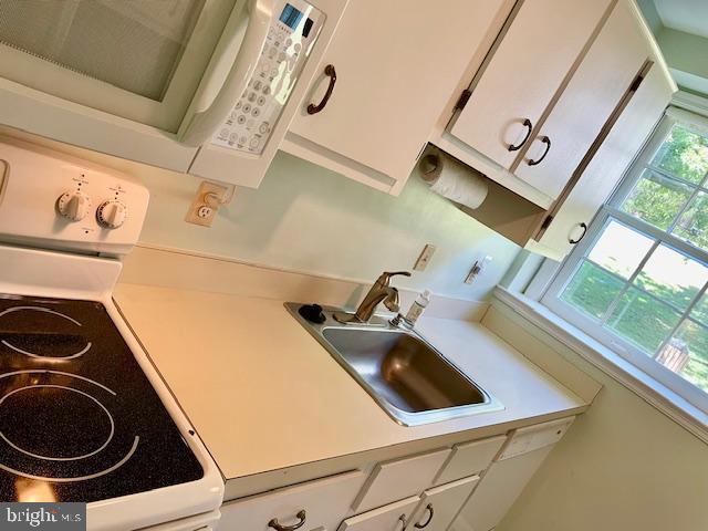 kitchen featuring white appliances, white cabinets, a sink, and light countertops