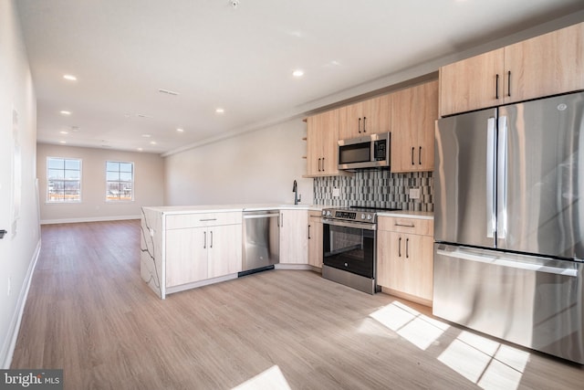 kitchen with a peninsula, appliances with stainless steel finishes, light brown cabinetry, and light wood-type flooring