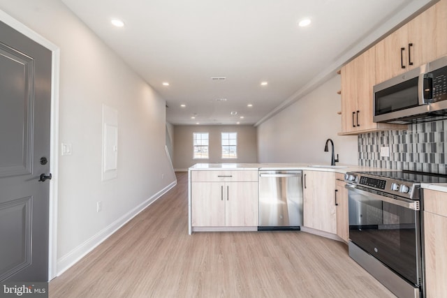 kitchen featuring stainless steel appliances, a peninsula, light brown cabinetry, and light wood-style floors