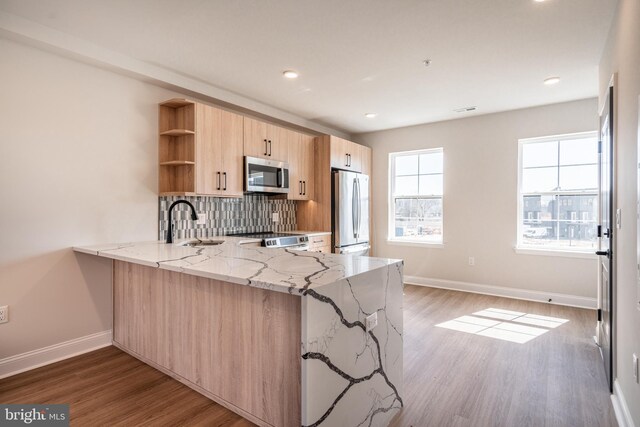 kitchen featuring light stone counters, open shelves, a sink, light brown cabinetry, and stainless steel appliances
