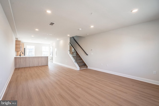 unfurnished living room with light wood finished floors, baseboards, and visible vents