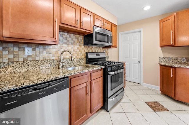 kitchen featuring light tile patterned floors, a sink, stainless steel appliances, light stone countertops, and tasteful backsplash