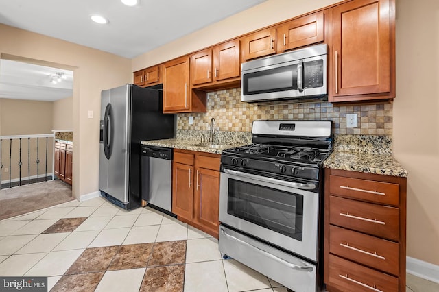 kitchen featuring brown cabinets, a sink, stainless steel appliances, baseboards, and decorative backsplash