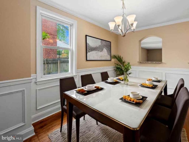 dining room featuring ornamental molding, an inviting chandelier, a decorative wall, a wainscoted wall, and wood finished floors