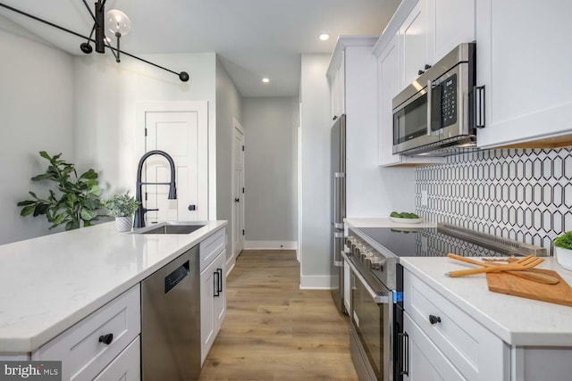 kitchen featuring recessed lighting, high end appliances, a sink, light wood-style floors, and white cabinetry