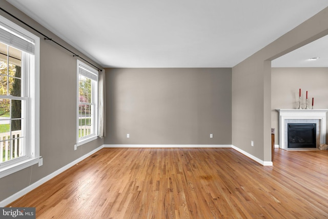 unfurnished living room with a fireplace with flush hearth, baseboards, and light wood-type flooring