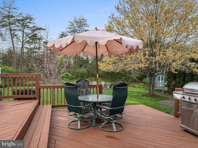 wooden terrace featuring outdoor dining area, a lawn, an outdoor structure, a storage unit, and a grill