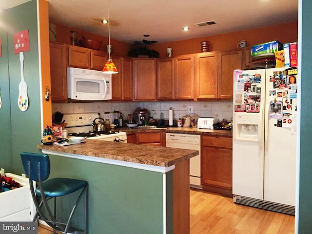 kitchen featuring a peninsula, backsplash, light wood-style flooring, and white appliances