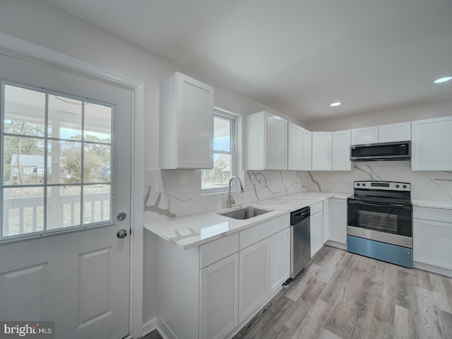 kitchen with light wood finished floors, white cabinets, a sink, and appliances with stainless steel finishes