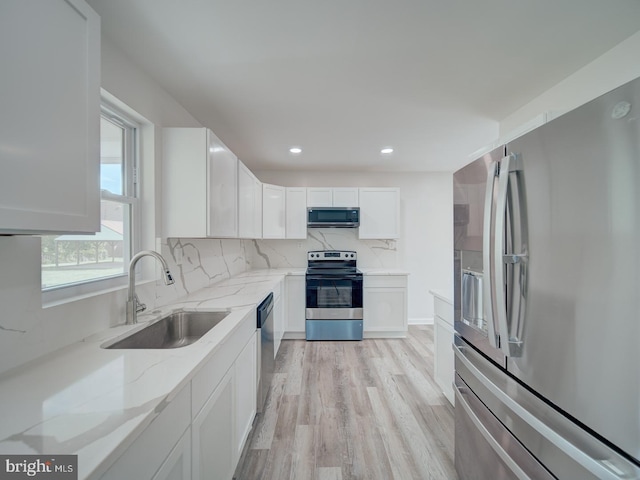 kitchen with light stone counters, a sink, light wood-type flooring, stainless steel appliances, and white cabinets