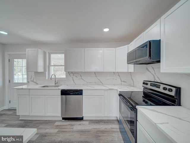 kitchen with light stone counters, a sink, light wood-type flooring, appliances with stainless steel finishes, and white cabinetry