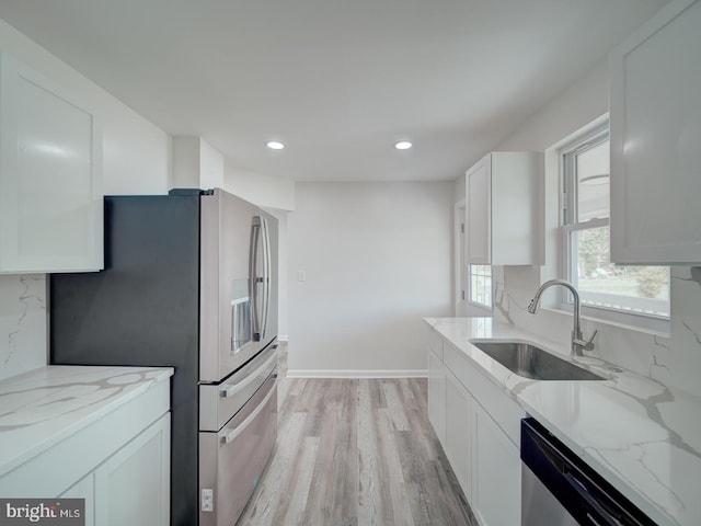 kitchen featuring light stone countertops, stainless steel appliances, a sink, and light wood finished floors